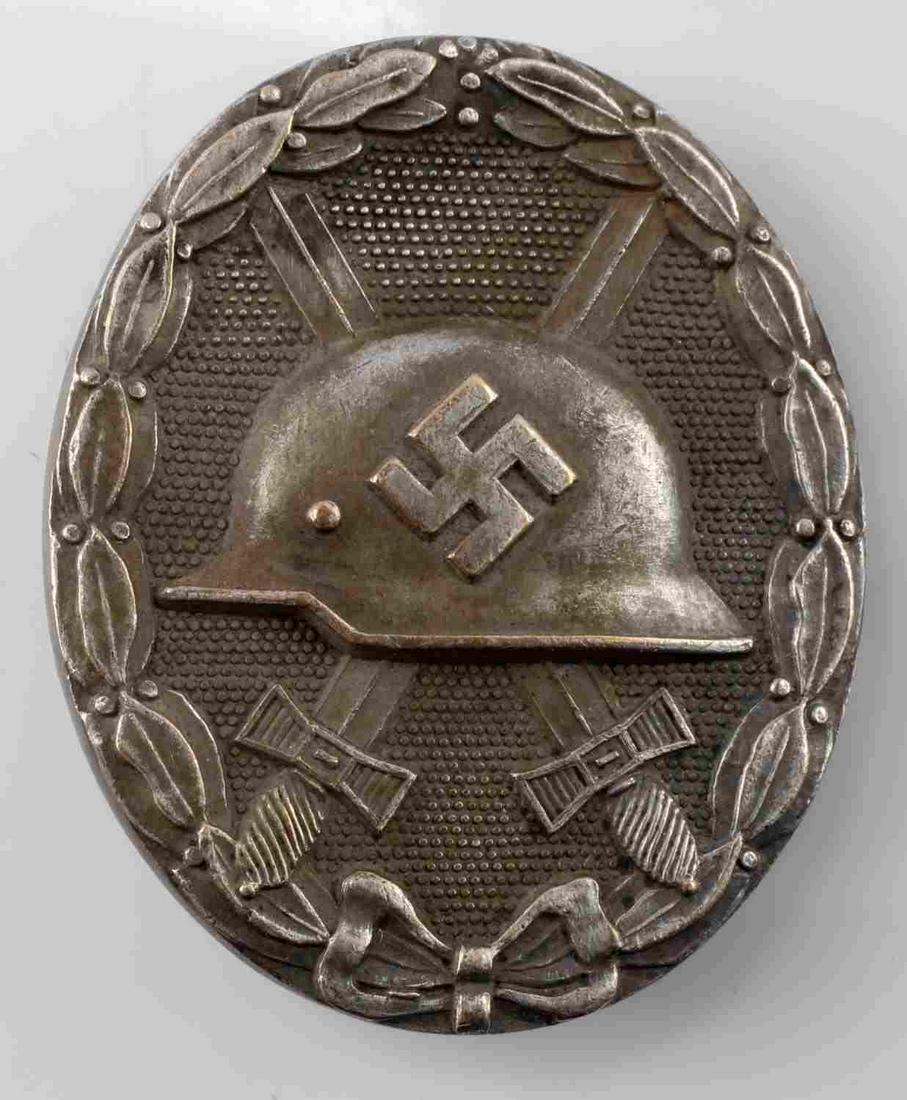 GERMAN WORLD WAR II SILVER WOUND BADGE: The front shows a German helmet in the center with a pair of crossed swords in the back ground. All three are surrounded by an oval oak leaf wreath. The reverse side is maker marked ‘30’. Has a wi