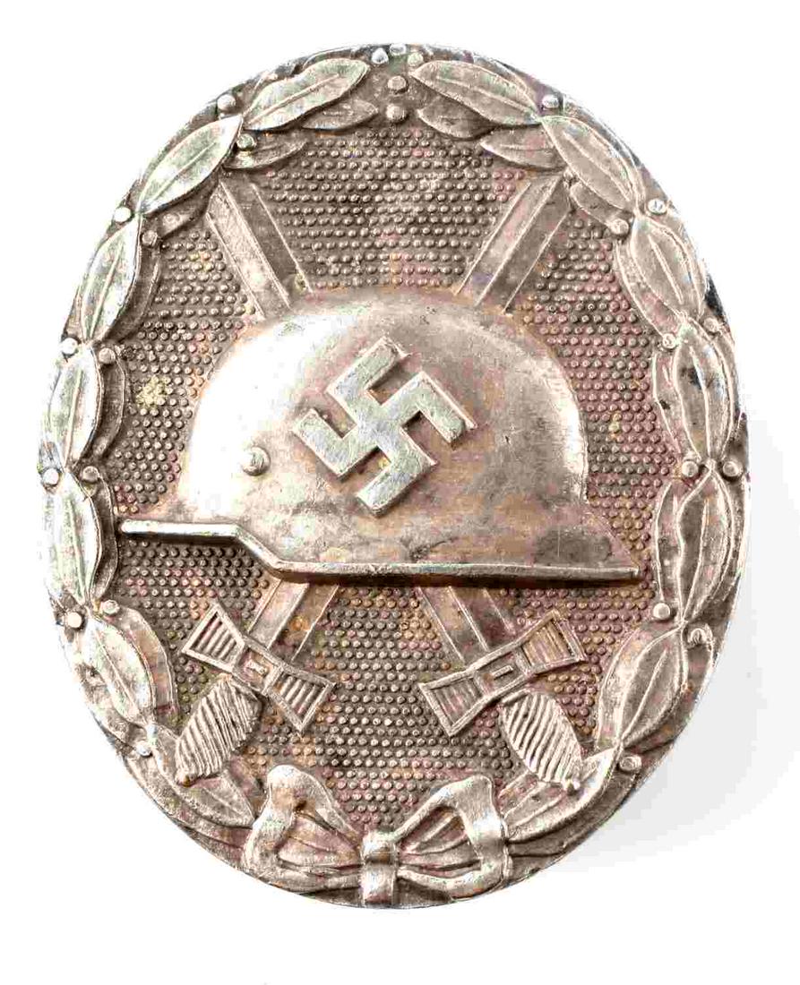WWII GERMAN THIRD REICH SILVER WOUND COMBAT BADGE: WWII German Silver Wound Combat Badge. The front shows a German helmet in the center with a pair of crossed swords in the background. All three are surrounded by an oval oak leaf wreath. The reverse s