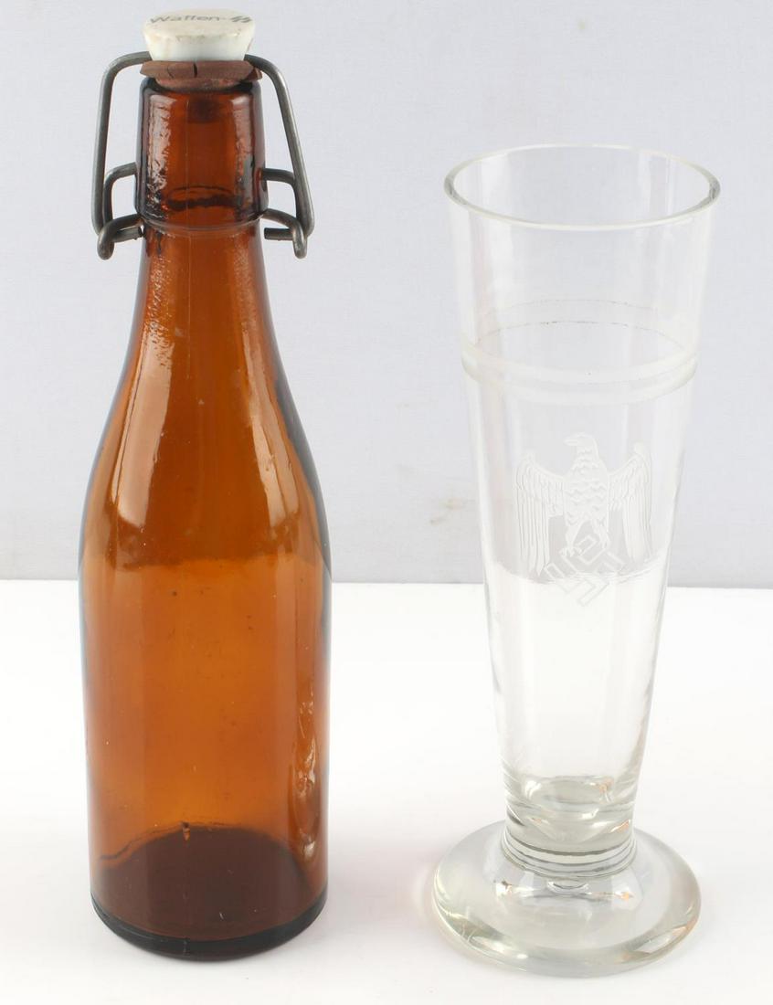 2 WWII GERMAN WAFFEN SS BEER BOTTLE AND BEER GLASS: WWII Waffen SS brown beer bottle and clear German beer glass. Brown glass bottle with clay cap marked "Waffen-SS". Appears to be marked to bottom. Measures 9 1/2 inches. Beer glass has two frosted lin