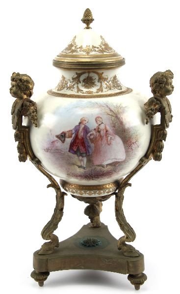 20TH CENTURY SEVRES PORCELAIN ORMOLU URN: 20TH CENTURY SEVRES PORCELAIN ORMOLU URN Porcelain urn, standing 16 inches tall with 18th century print design and gold decoration. Attached to an gilt metal frame with cherub finials and stand. The l