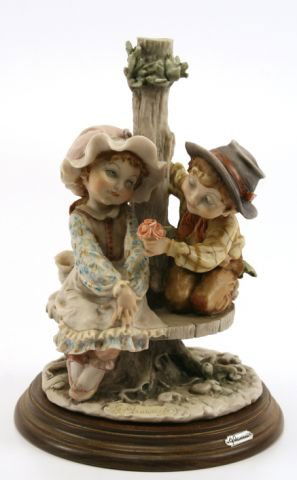 GIUSEPPE ARMANI STATUE BOY & GIRL ON BENCH: GIUSEPPE ARMANI STATUE BOY & GIRL ON BENCH A beautiful 11 inch Guiseppe Armani figurines depicting a young boy giving a girl flowers while sitting on a bench. Figurine is marked with blue N and crown