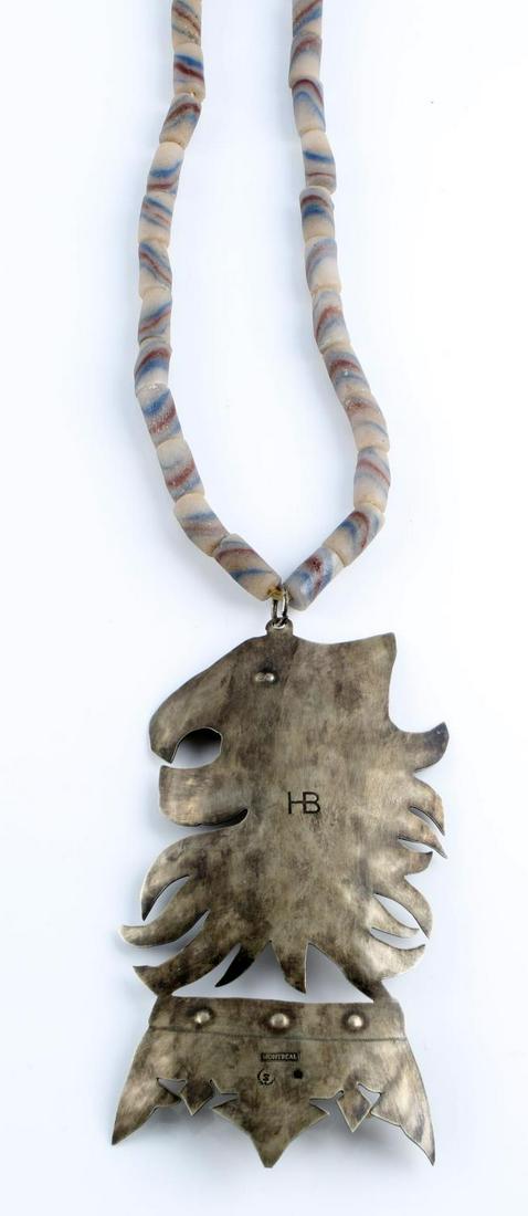 HUDSON BAY FUR TRADE BEAD AND GORGET MONTREAL: 6X3 inch white metal gorget with Lions Head effigy, stamped HB for Hudson Bay Company, Montreal and married to a strand of 2cm burgundy and blue striped trade beads.