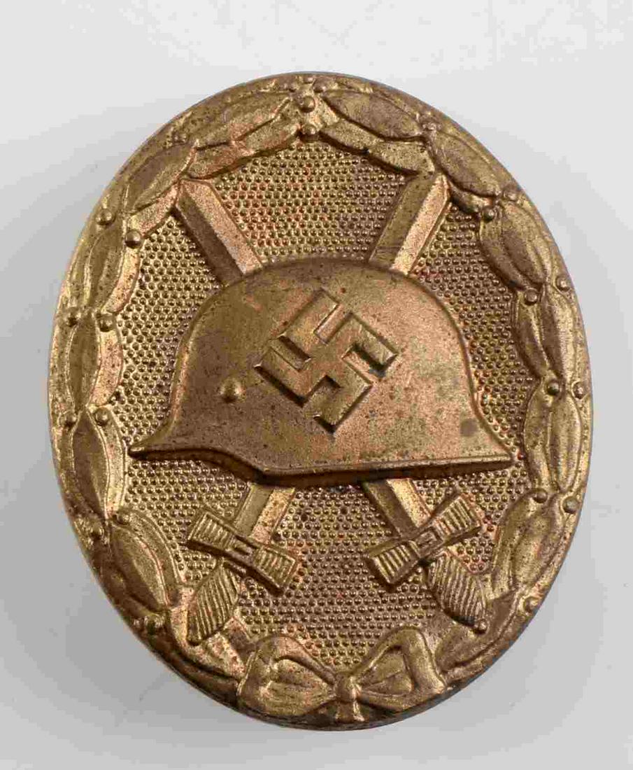 WWII THIRD REICH GERMAN WOUND BADGE GOLD TONE: The front shows a German helmet in the center with a pair of crossed swords in the back ground. All three are surrounded by an oval oak leaf wreath. The reverse side is maker marked ‘L/14’. Has a 