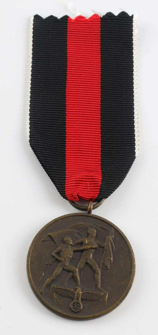 WWII GERMAN THIRD REICH CZECH ANNEX MEDAL: German WWII 1938 Czechoslovakian Annexation Decoration. Measures 1 1/4 inches in diameter. The front shows two men holding a flag with a German eagle below. The reverse side reads ‘Ein Volk – Ein 