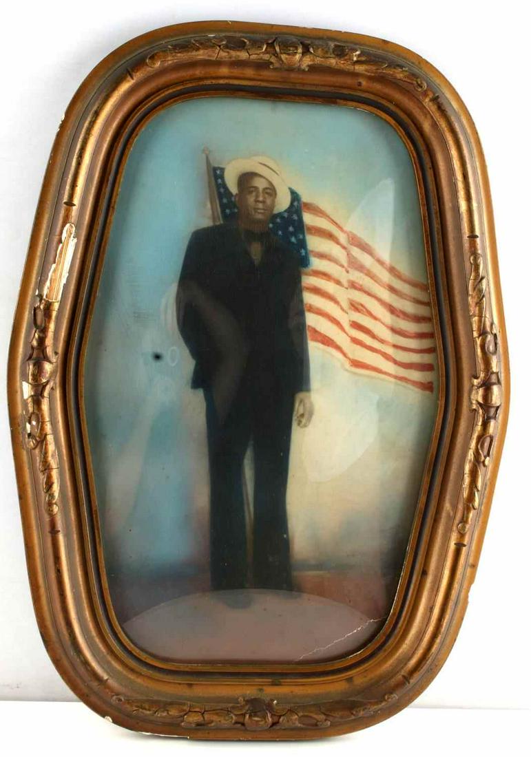 1900'S AFRICAN AMERICAN US FLAG TINTED PHOTO: Convex glass in Gesso frame that has some loss, hand tinted photograph of African American man in Boater style hat in front of 48 star U.S. Flag. lower right crack in photo. Measures 13 by 17 inches
