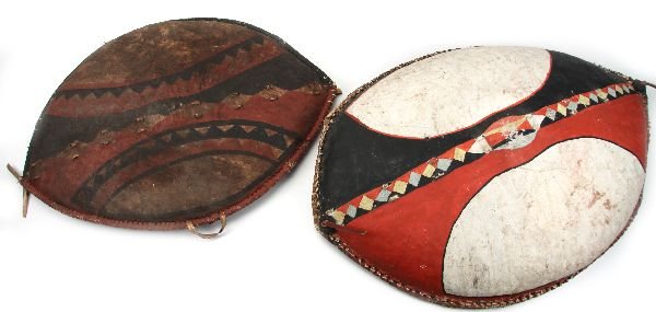 GROUPING OF TWO AFRICAN MAASAI TRIBAL SHIELDS: A beautiful pair of shields from the Maasai tribe of South-central Africa. These elliptical, convex shields are made from buffalo or cowhide stretched over wood. The patterns and designs of these shie