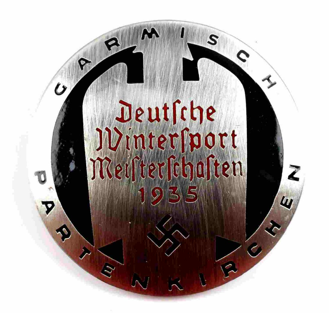 POST WWII PROD GERMAN REICH WINTER SPORTS BADGE: Post WWII production Third Reich Winter Sports 1935 badge. Black enamel on brushed steel. Deutsche Wintersport Meisterschasten. Measures 1 1/2 inches.