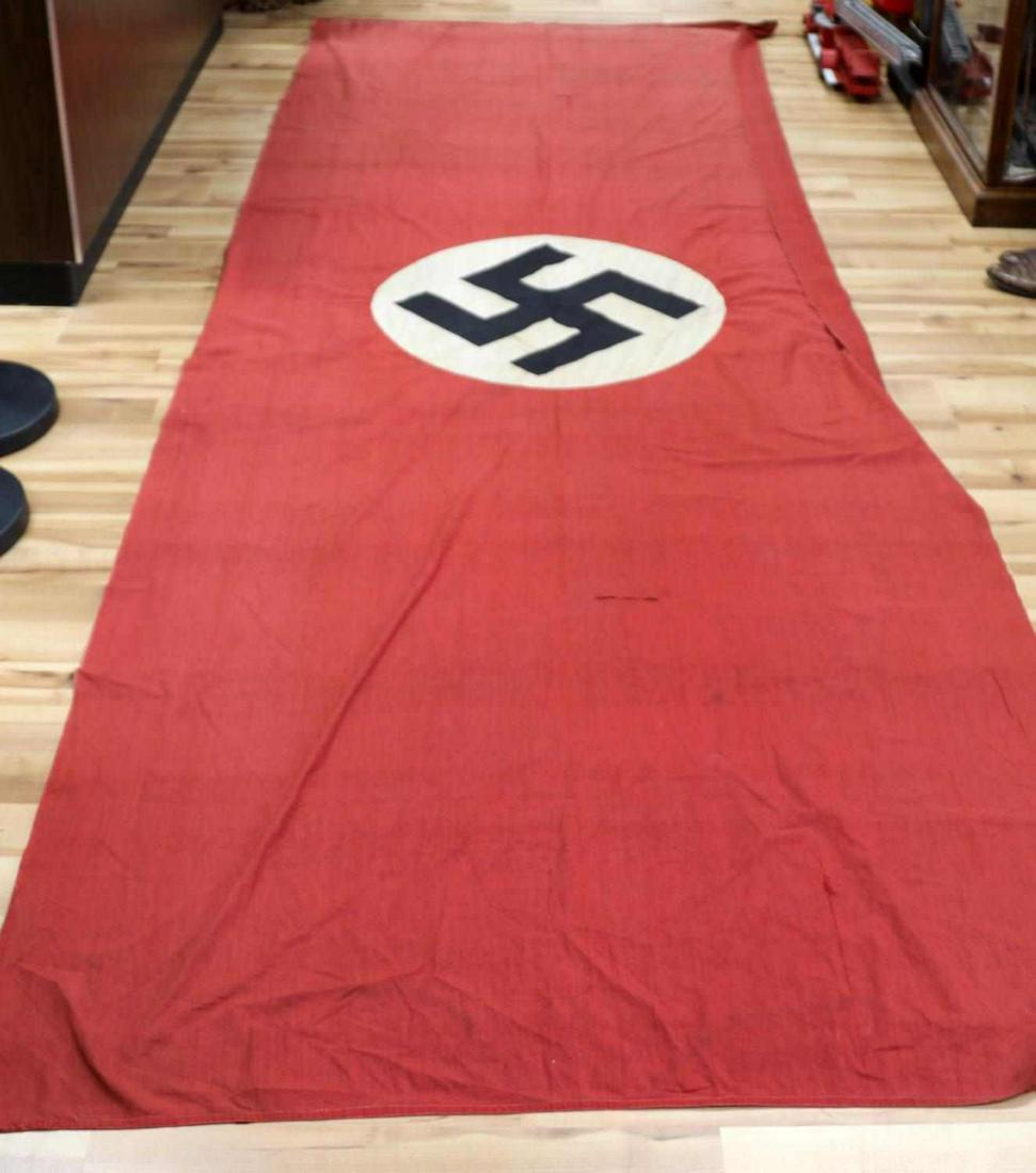 WWII GERMAN THIRD REICH 12 FOOT NSDAP BANNER FLAG: WWII German NSDAP building banner flag. Red cloth flag with white roundel to center with a black swastika. Some tearing and a patch work. Rope hangers to the end. Overall good condition. Does not fluo