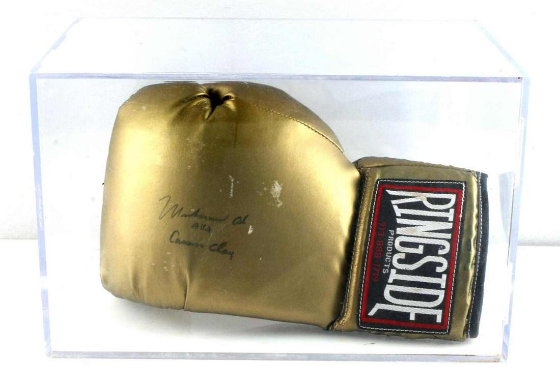 MUHAMMED ALI AUTGRAPHED RINGSIDE BOXING GLOVE: Gold Ringside boxing glove signed by Muhammed Ali. Signature in black ink reads "Muhammed Ali A.K.A. Cassius Clay". Some cracking to leather due to age. Signature still clear. Comes in plastic case. C