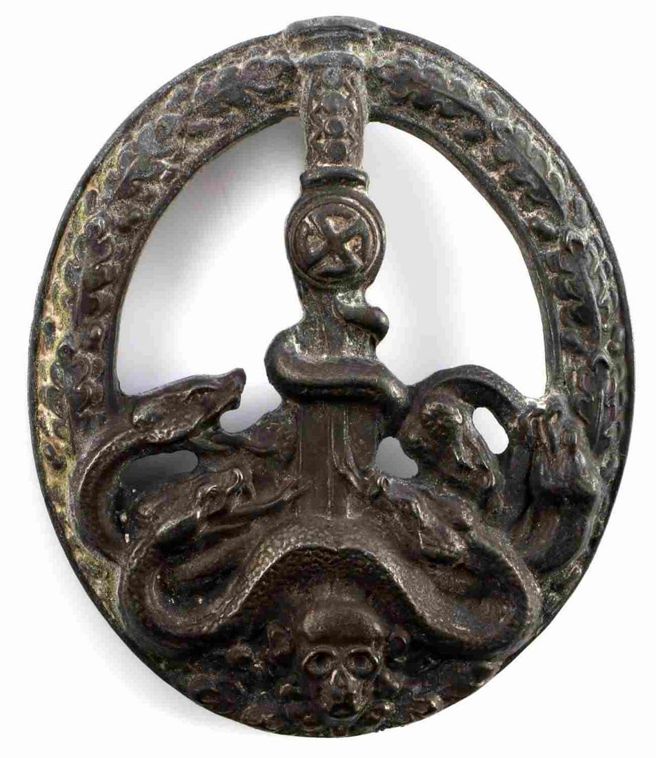 WWII GERMAN ANTI PARTISAN BADGE IN SILVER: WWII German silver anti-partisan badge. Obverse feature sword with sunwheel swastika to center stabbing a five-headed hydra below with a skull to the bottom. All surrounded by an oak leaf wreath. Thin