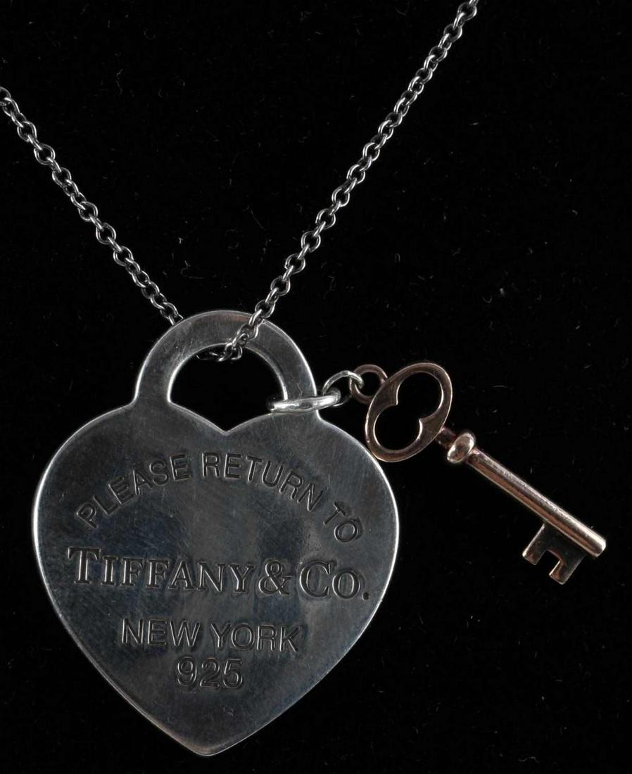 TIFFANY & CO HEART AND KEY STERLING NECKLACE: Front of heart reads "PLEASE RETURN TO TIFFANY & CO. NEW YORK 925" and measures 1 inch from bail to point of heart. "TIFFANY & CO. Ag 925" is stamped on reverse of heart. Key is attached to the bail o