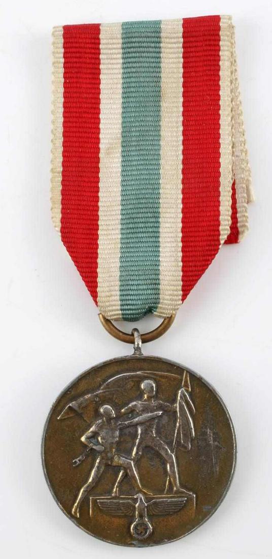 WWII GERMAN THIRD REICH MEMEL LANDS DECORATION: German World War II Military 1939 Memel Lands Decoration. Measures 1 1/4” inches in diameter. The front shows two men holding flags with a German eagle at the base. The reverse side reads ‘Zur Eri