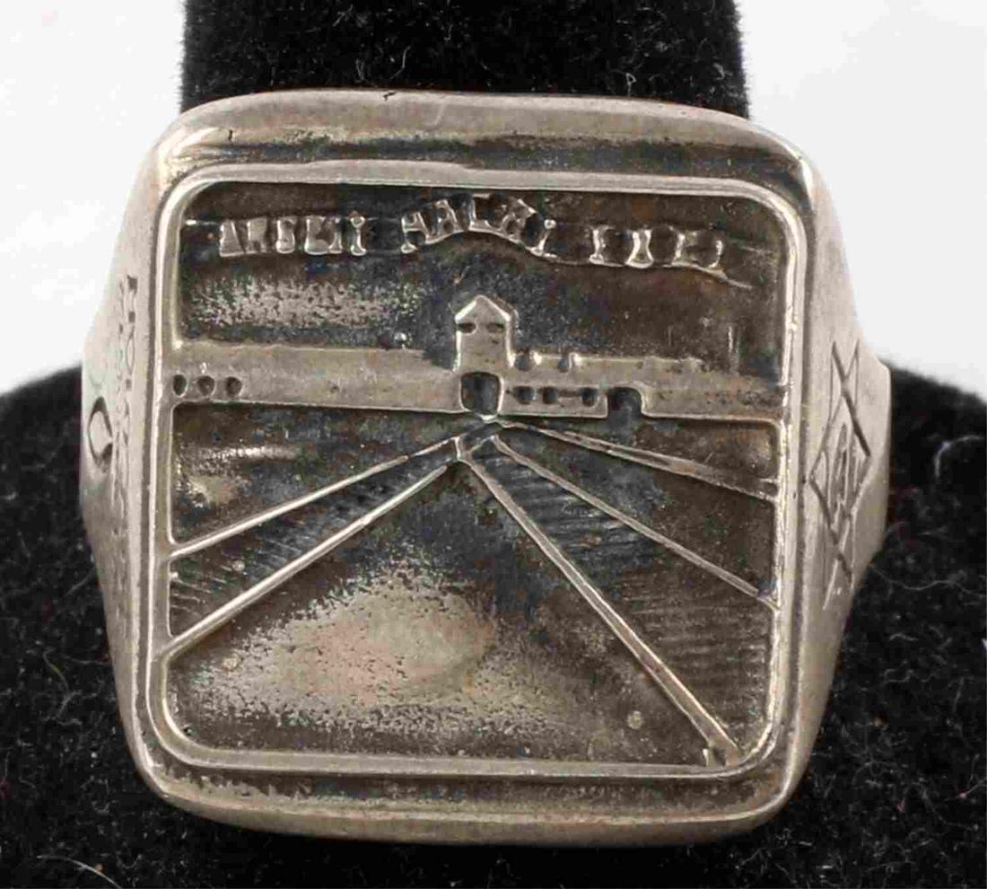EZI ZINO HOLOCAUST MEMORIAL AUSCHWITZ SILVER RING: Holocaust Memorial Ring designed by Ezi Zino. Size 10. Face features the entrance to Auschwitz with "Arbeit Macht Frei" ribbon above. Sides of the ring feature a Star of David with 'Jude' inside and "