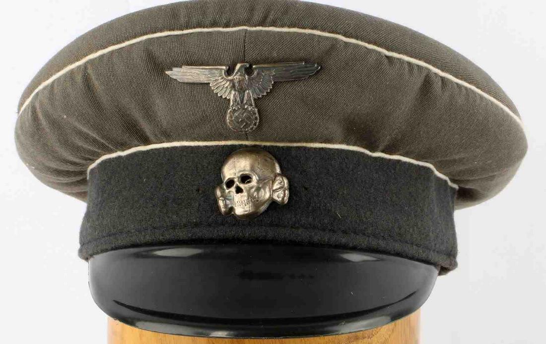 WWII GERMAN WAFFEN SS VISOR CAP: WWII German Waffen SS visor cap. Greenish-gray crown with a faded black band and a hard plastic visor. Totenkopf and eagle insignia unmarked. Interior size marked 57. Machine sewn brown leather sweatb