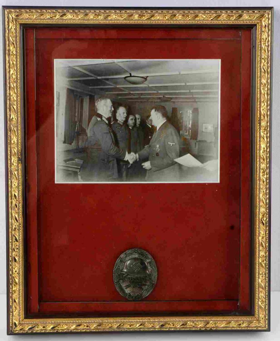 WWII GERMAN SS FRAMED BLACK 1944 WOUND BADGE: Framed German WWII Black July 20 1944 Wound Badge. Measures 1.5 inches wide by 1.75 inches tall. The front shows a German helmet with a pair of crossed swords in the background. Below reads “20 Juli