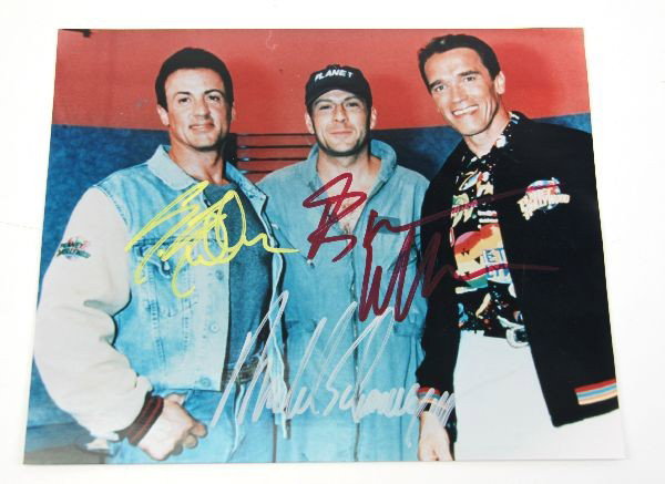 3 ACTION MOVIE CELEBRITY AUTOGRAPHS WITH COA: Autographed photograph of action movie actors Sylvester Stallone, Bruce Willis, and Arnold Schwarzenegger. COA from Showcases USA on back. Photo measures 9 3/4 by 8 inches. Very good condition.