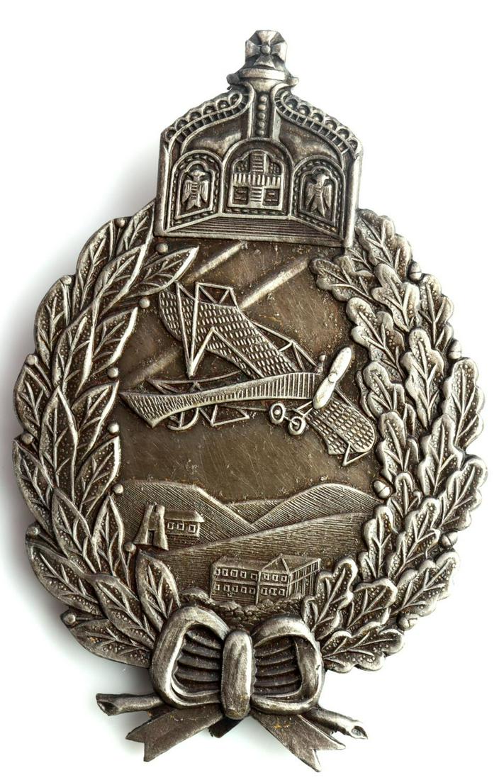 WWI IMPERIAL GERMAN PRUSSIAN PILOTS BADGE: Imperial German WWI Prussian Pilot Aviator Badge. Measures 1 11/16 X 2 13/16 inches. The front shows an airplane flying over farms and hills in the center. There is a King’s crown at the top with a 