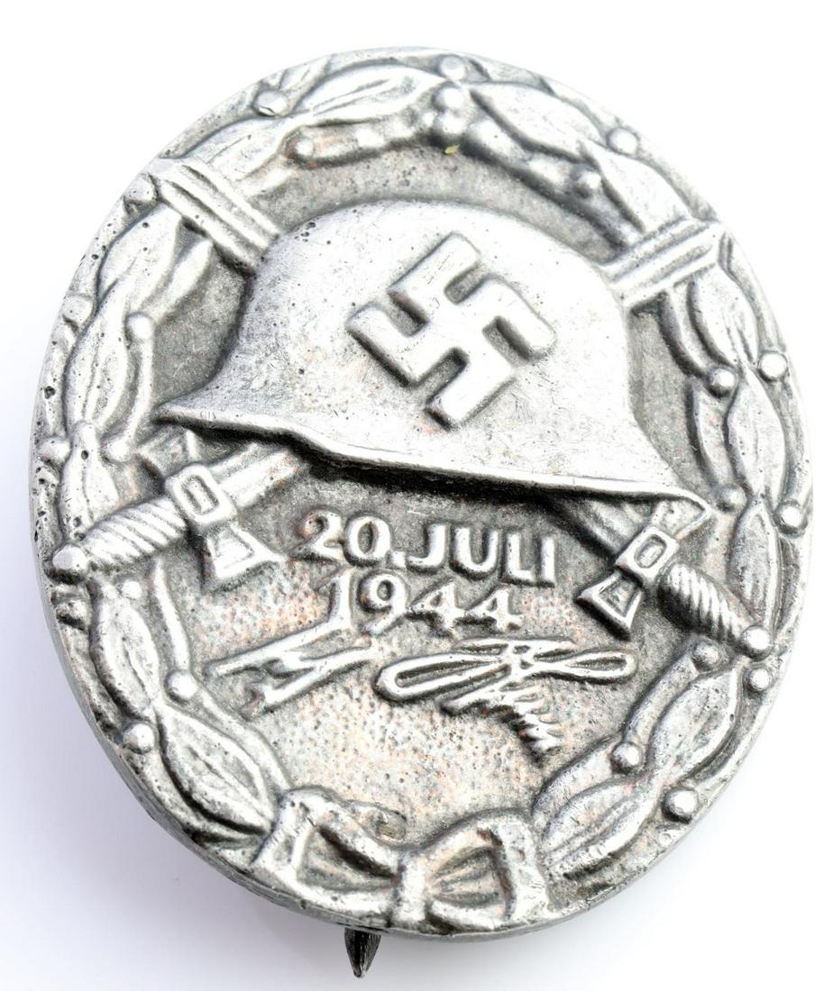 WWII GERMAN THIRD REICH SILVER 1944 WOUND BADGE: German WWII Silver July 20 1944 Wound Badge. Measures 1 1/2” wide by 1 13/16” tall. The front shows a German helmet with a pair of crossed swords in the back ground. Below reads ‘20 Juli 1944 Ad