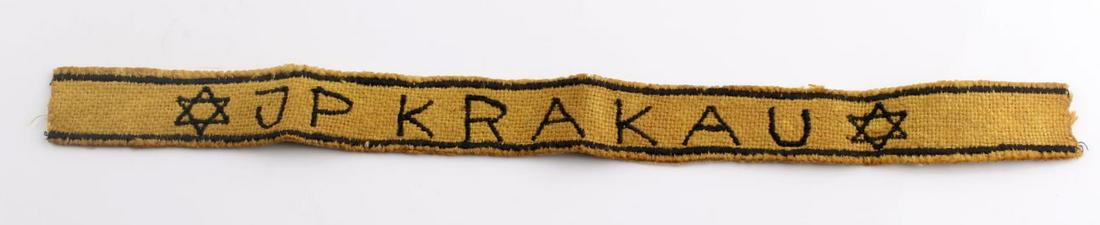 WWII GERMAN THIRD REICH KRAKAU CAMP ARMBAND: German WWII Jewish JP KRAKAU Concentration Camp Arm Band. Measures 9” wide by 2 7/8 inches tall. The front reads ‘JP KRAKAU’. There is a Jewish Star on the side. One piece machineembroidered and