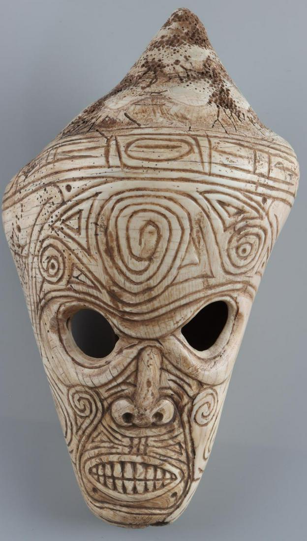 TAINO WHELK SHELL CARVING FULL FACE: Taino. C 800-1500 AD. A substantial shell head with completely engraved face. Eyes are carved through the shell. The nose resembles a phallus, volutes circle just under eyes. A complex system of bird 