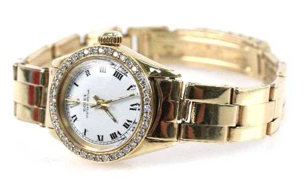 LADIES 18K ROLEX OYSTER PERPETUAL W/DIAMOND BEZEL: Ladies 18K yellow gold Rolex Oyster Perpetual watch with diamond bezel in box. Some surface wear to face (18 mm) and band, band measures 7 inches and has some slack. Weight: 53.2 Condition: Very good