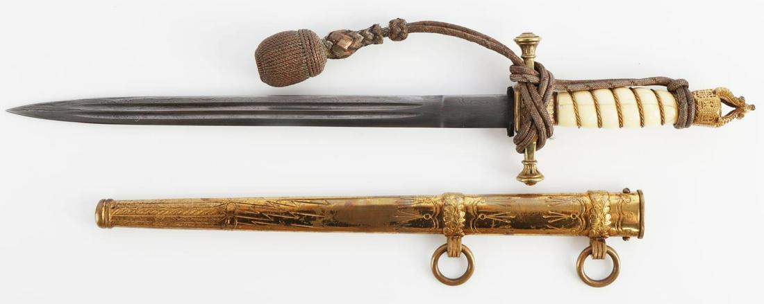 WWI IMPERIAL GERMAN NAVY DAMASCUS DAGGER TUSK GRIP: Damascus steel blade with tusk grip, brass crossguard, and brass pommel. Housed in brass scabbard. Button marked 14kt. Tang engraved 86473. WKC mark. Measures 15 inches. Comes with portepee. Very fine