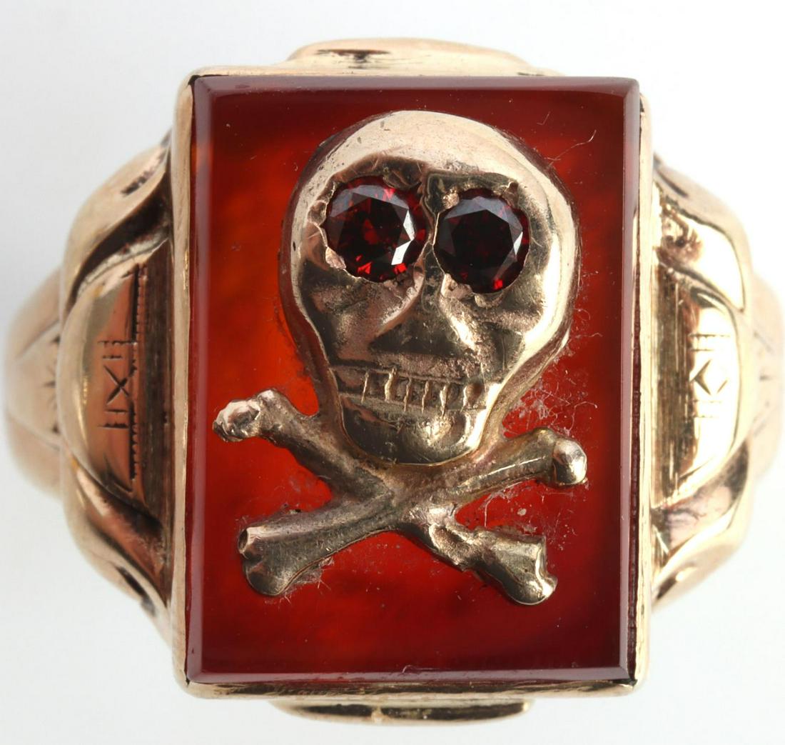 10KT GOLD SKULL AND CROSSBONES SIGNET RING: 10kt yellow gold ring with Carnelian center stone adorned with gold skull and crossbones with ruby eyes. Size 13. Total weight of 7.6 grams. This lot has a reserve.