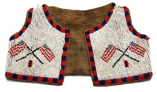 NATIVE AMERICAN BEADED CHILDS VEST WITH FLAGS: Antique Red, white, and blue trade beads attached to a small hide vest. Crossed American flags on field of white to each front panel. Border in alternating red and blue. Back has red and blue trim and