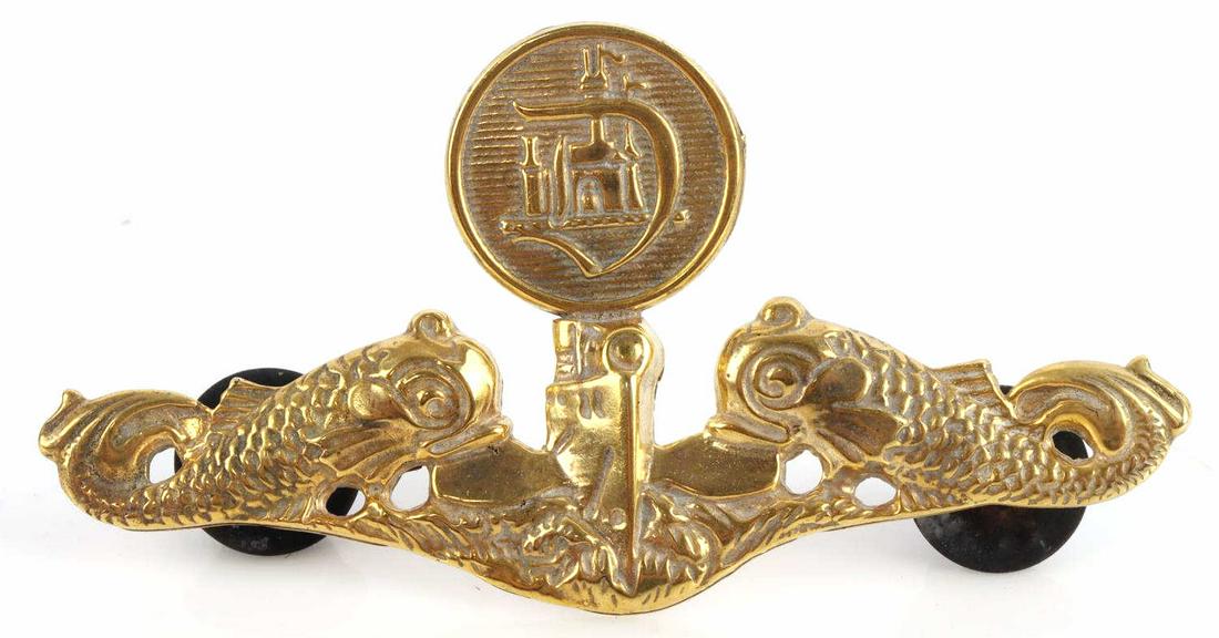 DISNEY VINTAGE DISNEYLAND SUBMARINE EMPLOYEE BADGE: Measures 2 11/16 inches wide by 1 3/8 inches tall. The front shows a submarine in the center flanked by a dolphin on each side. Aboveis a round button with a ‘D’ that has the Disneyland castle in 