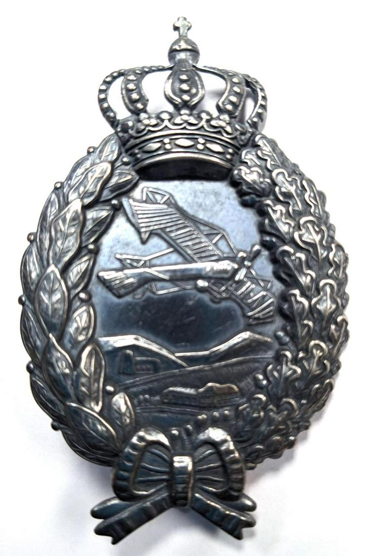 WWI IMPERIAL GERMAN AVIATOR PILOT BADGE: Imperial German World War I Aero Bavarian Aviator Pilot Badge. Measures 1 3/4 X 2 3/4 inches. The front shows an airplane flying over some buildings and small mountains in the center. They are all sur