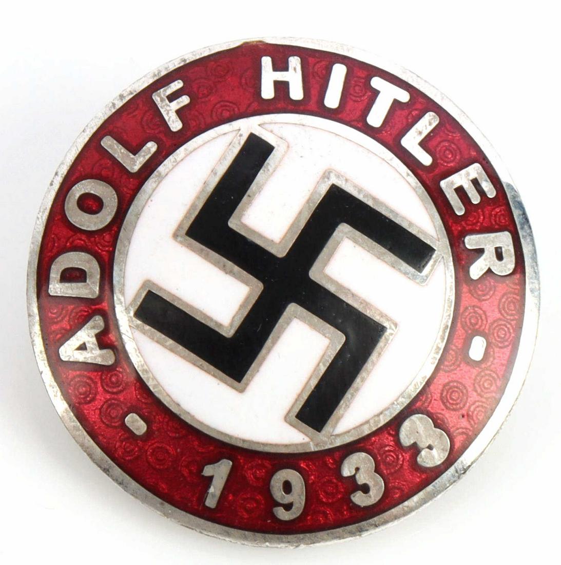 WWII GERMAN ADOLF HITLER 1933 SWASTIKA LAPEL BADGE: Measures 1 inch in diameter. The front reads ‘Adolf Hitler 1933’. There is a swastika in the center. The reverse side is maker marked ‘RZM M1/129’. Has a thin horizontal safety pin back. One p