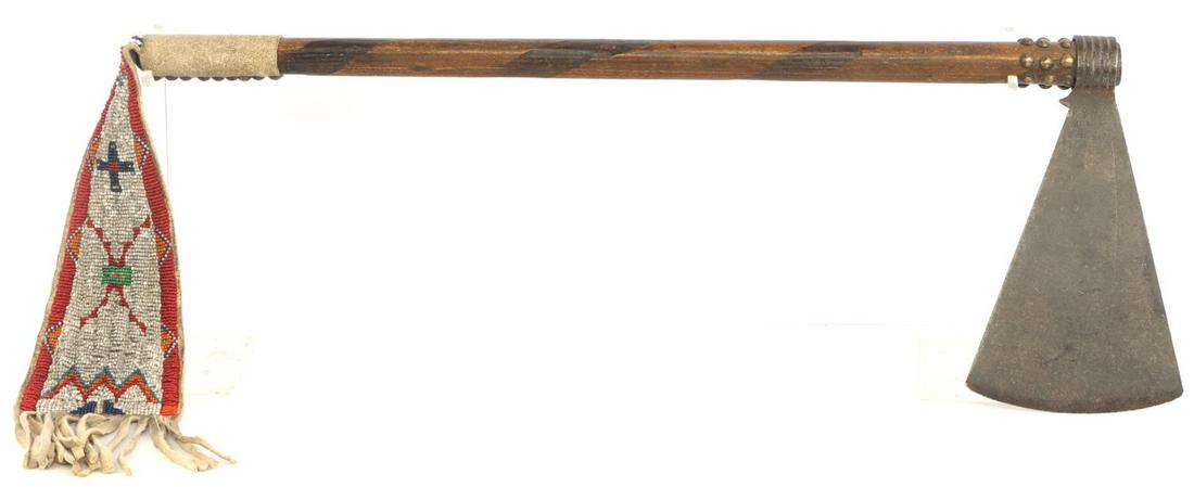 19TH CENTURY MISSOURI WAR AXE NATIVE AMERICAN: Wrought steel axe head with wooden shaft. Shaft embellished with brass half beads with an alternating strip pattern. Attached to the base is a leather pennant with intricate bead work. Axe head measur