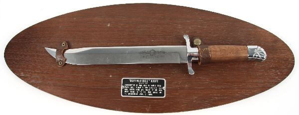 BUFFALO BILL COMMEMORATIVE KNIFE: Decorative Buffalo Bill reproduction knife on wooden plaque. Features a written description which reads, "A reproduction of a knife used by a famous Great plains scout William F. Cody (1846-1917) pony