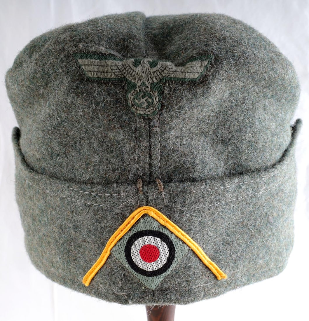 WWII GERMAN THIRD REICH OVERSEAS OFFICER CAP: Field grey cap with Heer eagle patch and cockade patch. Features fading from age. Non-fluorescing. Ink stamp on interior numbered 0049/7472/16080. It measures 11 1/2 inches. Unauthenticated, sold as i