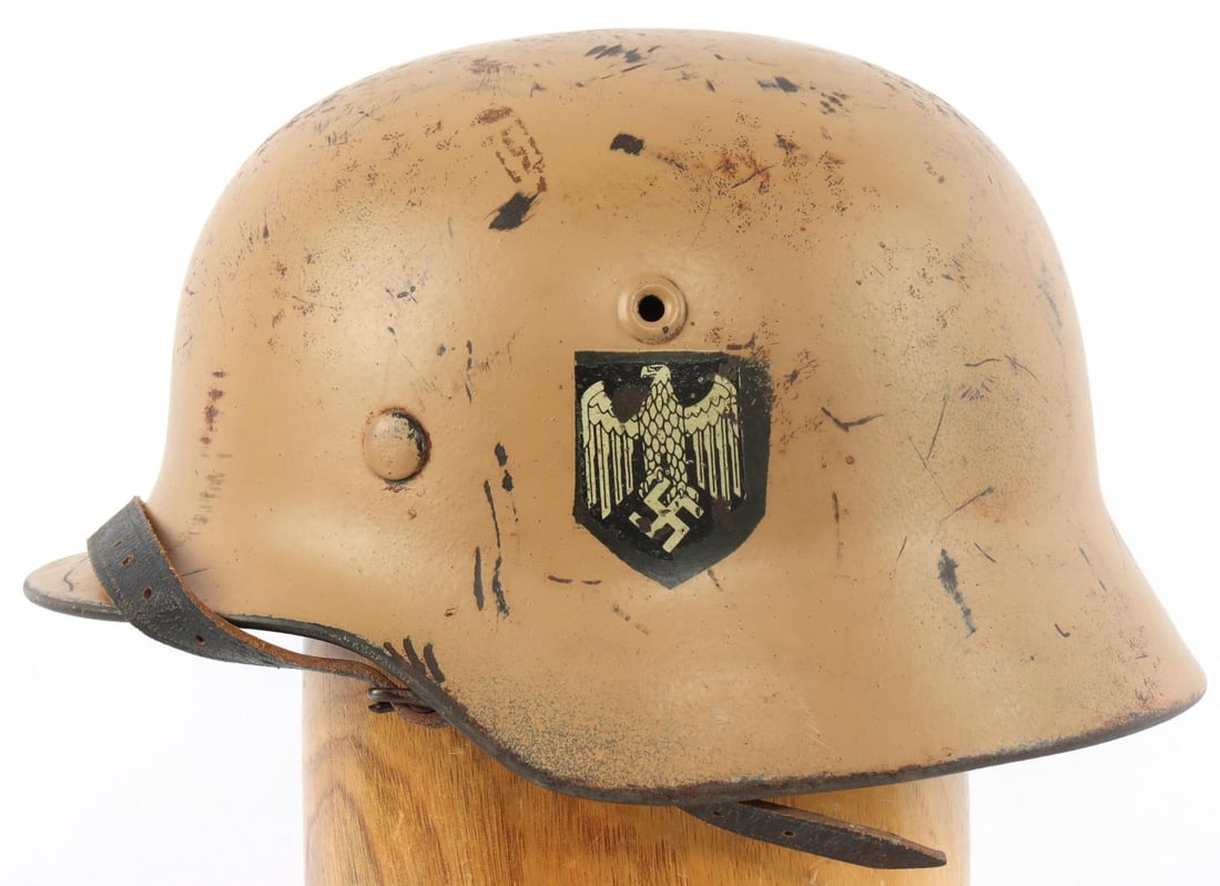 WWII GERMAN REICH M40 AFRIKAKORPS STAHLHELM: With Afrikakorps tan paint. About 60% of finish on exterior, Heer decal on left appears to have been poorly done. Liner and chinstrap in good condition. "ET62" on left interior of helmet, "541" on rea