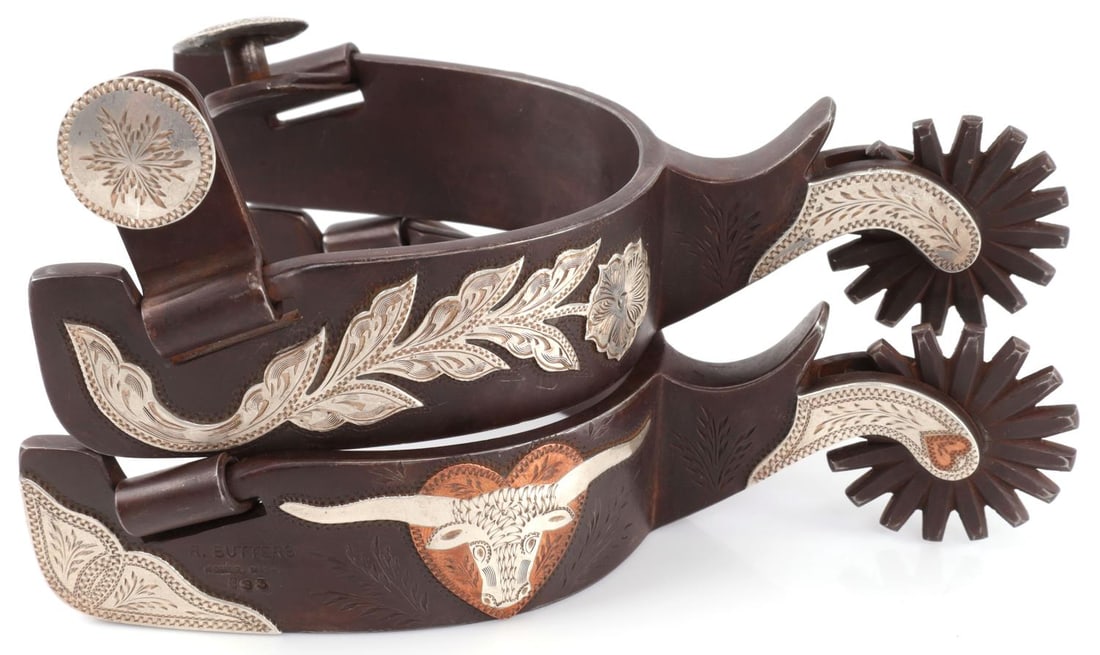 DOUBLE MOUNTED RANDY BUTTERS TEXAS STYLE SPURS: Pair of double mounted Randy Butters silver inlaid Texas Style spurs. Heel bands feature silver inlaid designed of a longhorn, hearts, and a flower. Exterior of the heel band features a manufacturer s