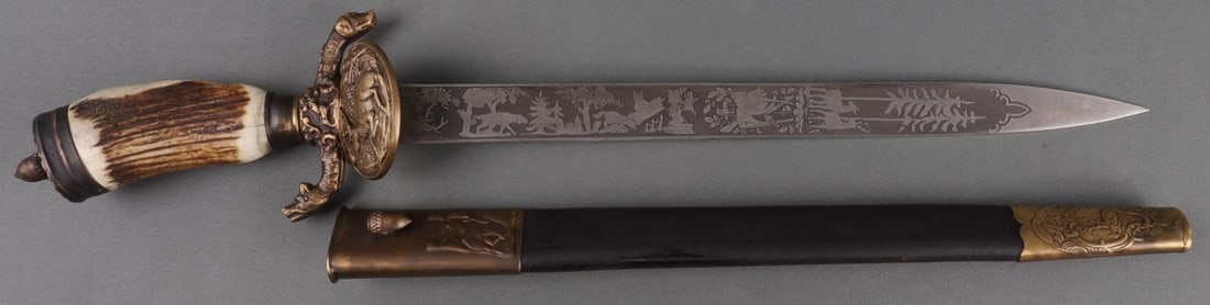 WWII GERMAN THIRD REICH HUNTING ASSOCIATION DAGGER: Blade has animal and forest imagery on one side, the phrase ' Got Mitt Uns' on the other. Stamped 'Solingen' and 'Alex Coppel.' Brass clamshell guard and antler hilt. Brass and leather scabbard. Blade