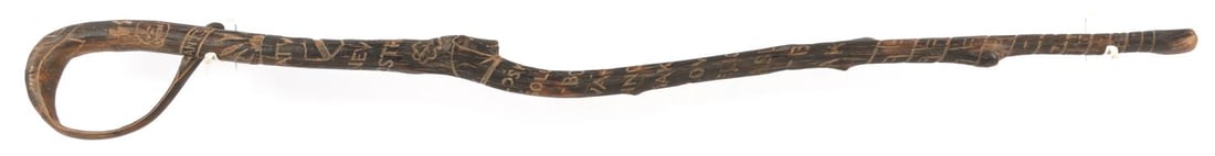 WWII GERMAN THIRD REICH SS LATVIA WALKING STICK: SS Walking Stick carved from wood. Top of cane has a carved Totenkopf and SS sig-runes, before moving down to a depiction of a sunrise or sunset over an inscription reading "LATVIJA - NEVEL OSTROV." U