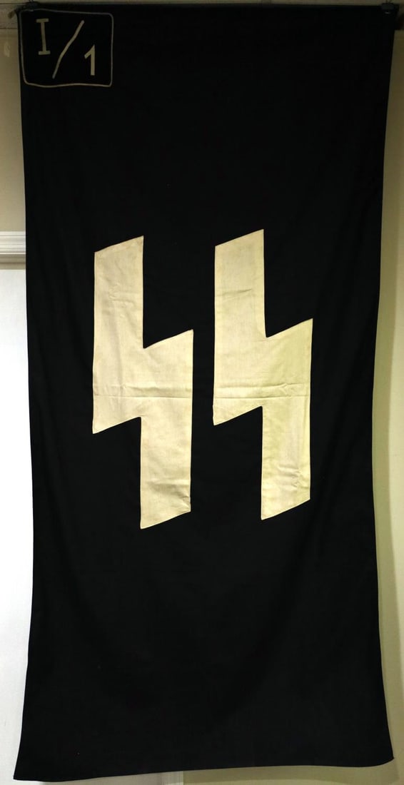 WWII GERMAN THIRD REICH LARGE SS FLAG: Large SS flag. Black cloth with white SS-runes. Short-hair wool patch in corner with L/1 logo. With mount. Multi-piece construction. Non-fluorescing. Black material with SS sig-runes in the center. 82