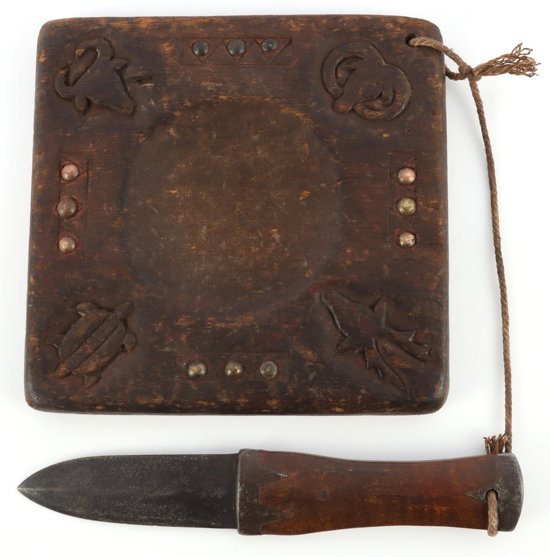 NORTH AMERICAN FUR TRADE CUTTING BOARD WITH KNIFE: Rustic cutting board with attached knife. Cutting board shows a mix of geometric and animal designs, with a goat, deer, turtle, and cow in each corner. Each triangle within the geometric design is mar