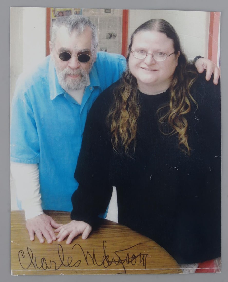 CHARLES MANSON SIGNED PRISON PHOTOGRAPH: Photograph of Charles Manson in prison standing next to a woman. Signed by Manson on the bottom. Deemed authentic according to terms.