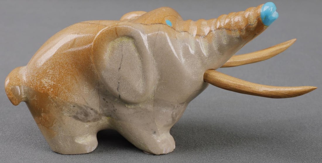 NATIVE ZUNI ANIMAL FETISH ELEPHANT: Zuni animal fetish depicting an elephant. Carved from travertine with turquoise aspects. Wooden tusks. Signed on bottom 'EL' for Zuni carver Enrike Leekya. 3.5 inches. Very good, original condition.