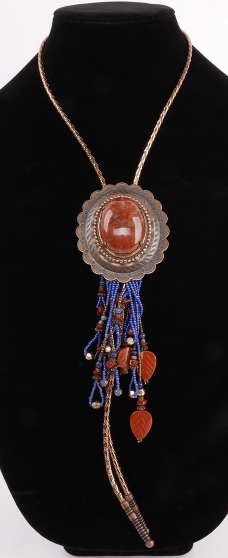 NATIVE AMERICAN NAVAJO APPLE CORAL & BEAD BOLO TIE: Copper bolo tie with large apple coral stone center piece. Blue and coral beadwork hanging from bottom. One (1) apple coral charm is split horizontally. 37-inch rope. Good, original condition.