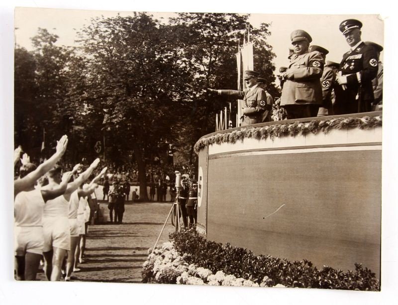 NSDAP HITLER AT SA SPORTS EVENT PRESS PHOTOGRAPH: 8.75 by 6.5 inch press photograph of Adolf Hitler, Hermann Goring, Hans Lammers, and other Nazi officers. The reverse of the photo is marked with a torn tag and an Atlantic Photo stamp. The photo show