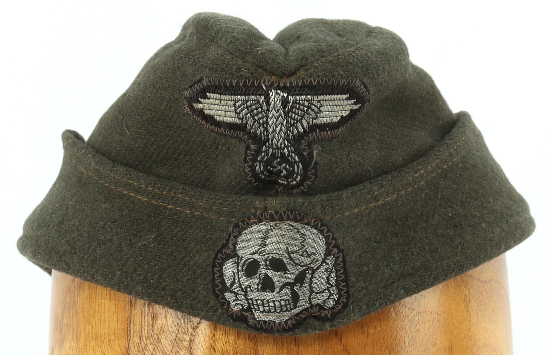 WWII GERMAN THIRD REICH SS OVERSEAS SIDE CAP: Overseas side cap for the Waffen-SS. Dark field gray construction with a lighter gray interior. Dark yellow stitching. Silver bullion threead Waffen-SS Reichsadler and Totenkopf. Non-fluorescing. Stam