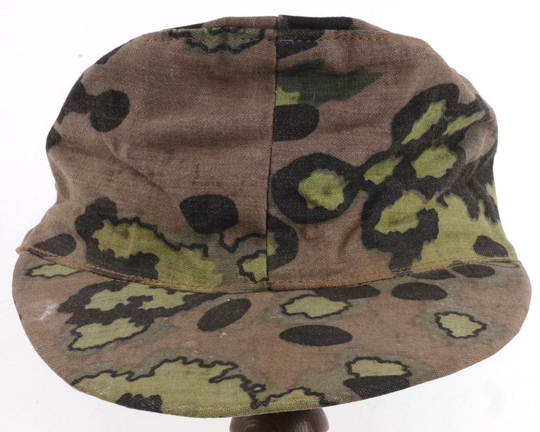 WWII GERMAN SS REVERSIBLE CAMO FIELD CAP: Reversible summer & fall camouflage pattern cotton twill. Without air vents. Interior ink stamped "Gesellschaft Textil GmbH DWB R 44." Good condition. Some fading, staining. Fabric does not fluoresce 