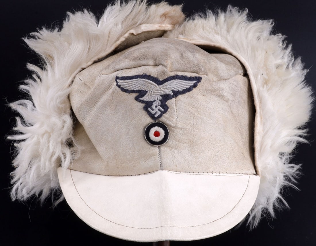 WWII GERMAN LUFTWAFFE COLD WEATHER RABBIT FUR HAT: Luftwaffe cold weather cap with ear flaps. Exterior of sheepskin. Interior has shaggy rabbit fur liner. Front of cap has embroidered eagle insignia over roundel. Underside of visor lined with gabardin