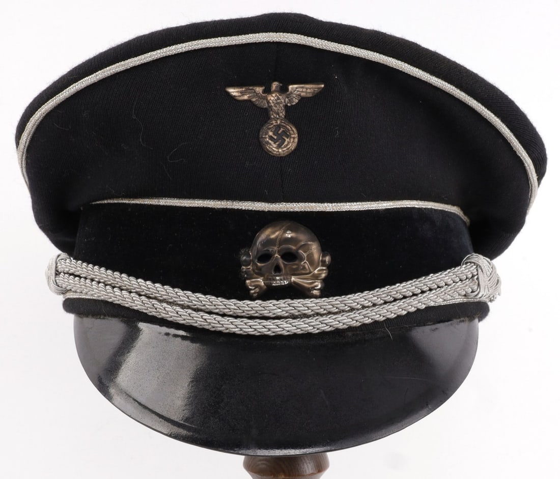 WWII GERMAN THIRD REICH HANS ZAHEL SS VISOR: Black visor with silver bullion strap, bearing early pattern totenkopf and Reichsadler pins. SS RZM tag under leather band. SS RZM stamp on visor. Interior tag reads J.B. Holzinger Uniformen Berchtesg