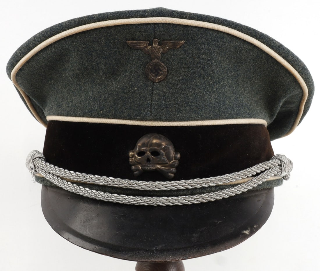 WWII GERMAN THIRD REICH SS OFFICER VISOR TYPE 1: Waffen SS visor with type 1 pins. Primarily field-gray in construction, with white piping and silver bullion strap. Aug Muller make. Non-fluorescing. Hat has been crushed or bent at some point, but is