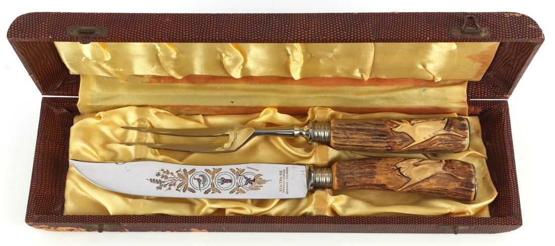 KLA TRA SO CASED MEAT CARVING SET KNIFE & FORK: Carving set from Kla Tra So, encased within a presentation box. Both pieces have finely carved antler handles, and the blade/prong are lightly engraved with forestry scenes. Forged in Solingen, German